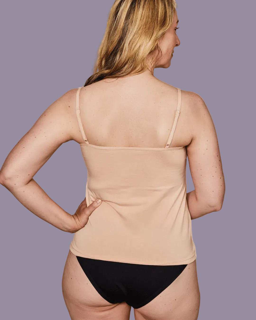 Woman wearing a beige tank top and black underwear on a purple background