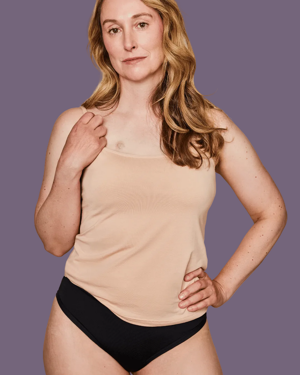 Woman wearing a beige tank top and black underwear on a purple background